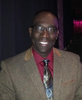 Man smiling in a brown jacket and red shirt
